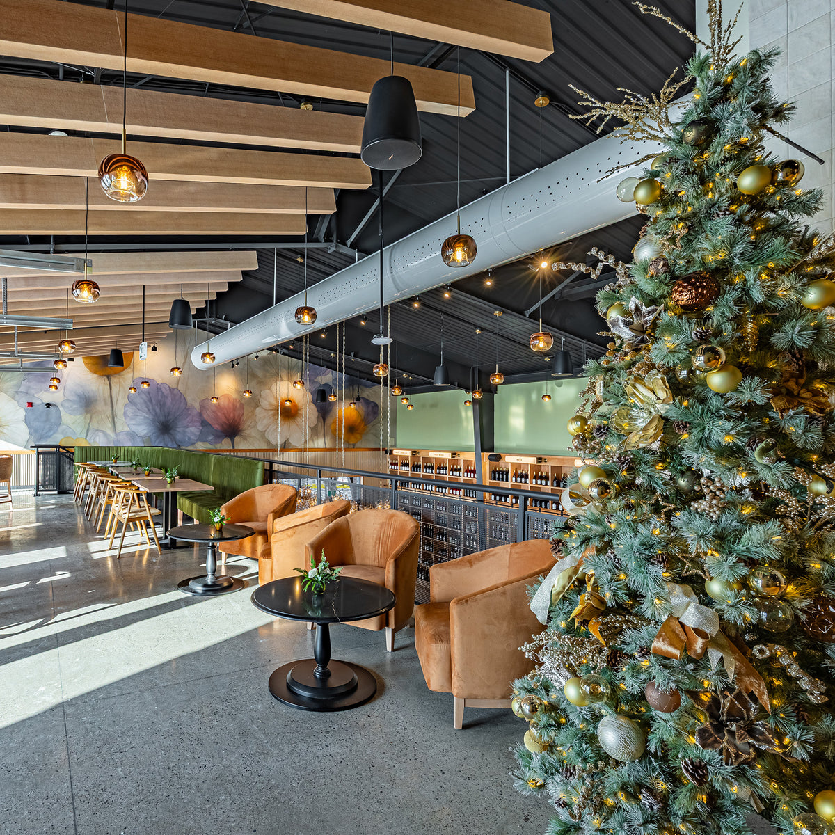 A decorated Christmas tree with gold ornaments stands in a Skye Chase mezzanine area with tan armchairs, small round tables, exposed ceiling beams, and pendant lights.